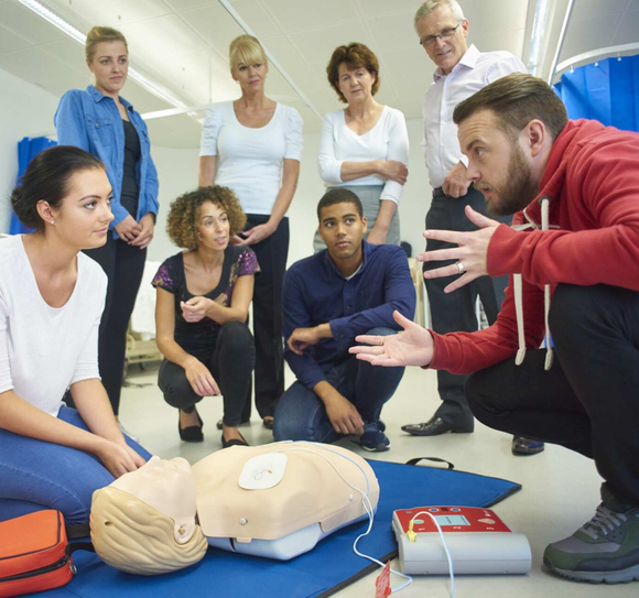 A group of people are sitting around a mannequin with a defibrillator on it