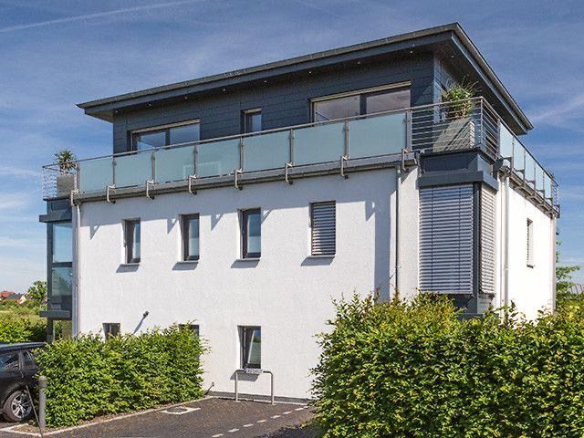 Modernes weißes Mehrfamilienhaus mit dunkelgrauem Dach und Glasbalkonen.