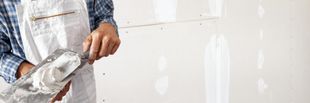 Person applying plaster to a white wall with a trowel