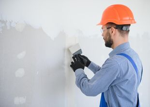 Worker in orange hard hat smoothing drywall with a putty knife on a white wall