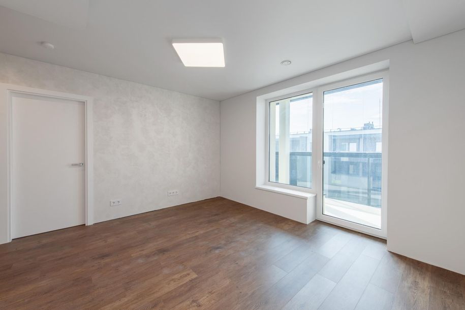 Empty modern room with wood floors, white walls, and large windows opening to a balcony.
