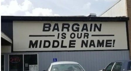 Storefront sign reading “BARGAIN IS OUR MIDDLE NAME!” with cars parked below