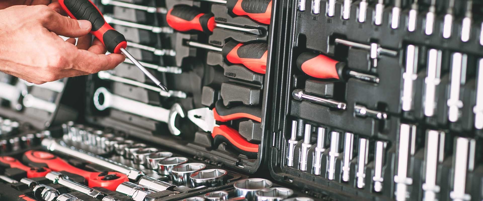 Hand holding tools in a red-and-black tool case with assorted wrenches and screwdrivers