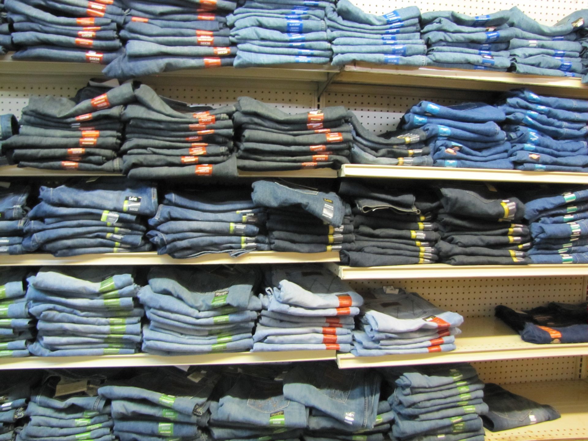 Shelves stacked with folded jeans and pants in blue, gray, and black shades in a store.