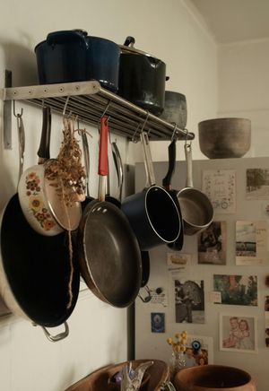 Kitchen wall rack with hanging pans and pots above a countertop cluttered with photos and notes