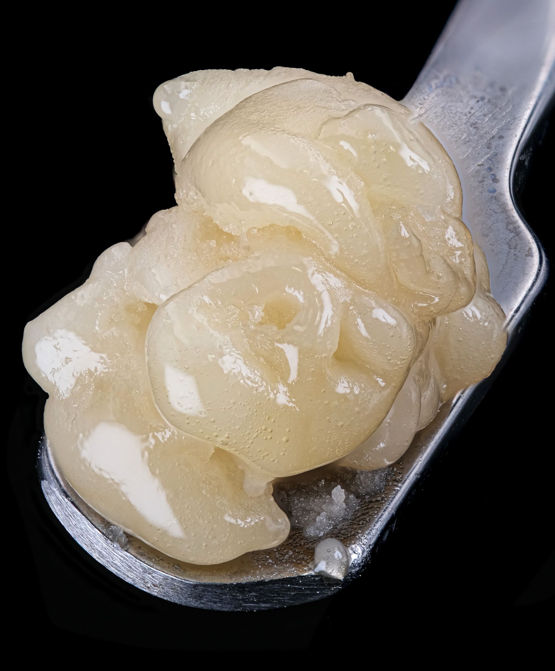 Dab of light yellow cannabis concentrate on a metal tool, against a black background.