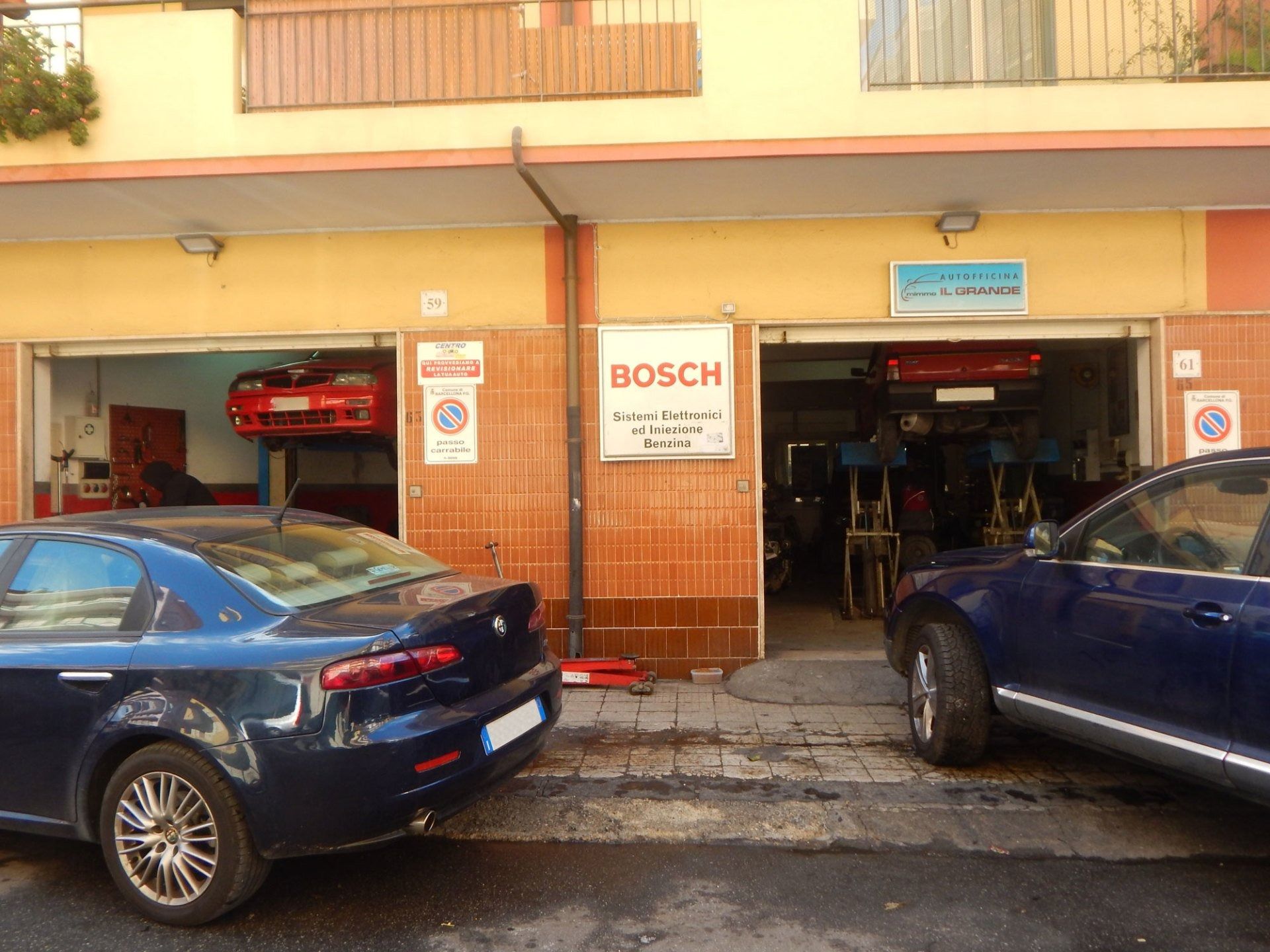 Car repair shop storefront with two blue cars parked outside and a Bosch sign above the entrance