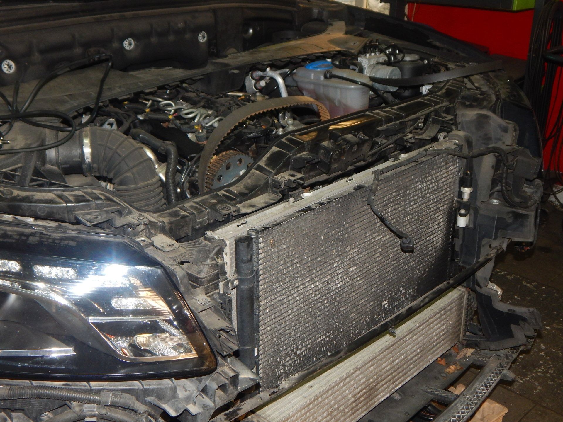Damaged black car front end in a garage, with hood open and exposed engine components