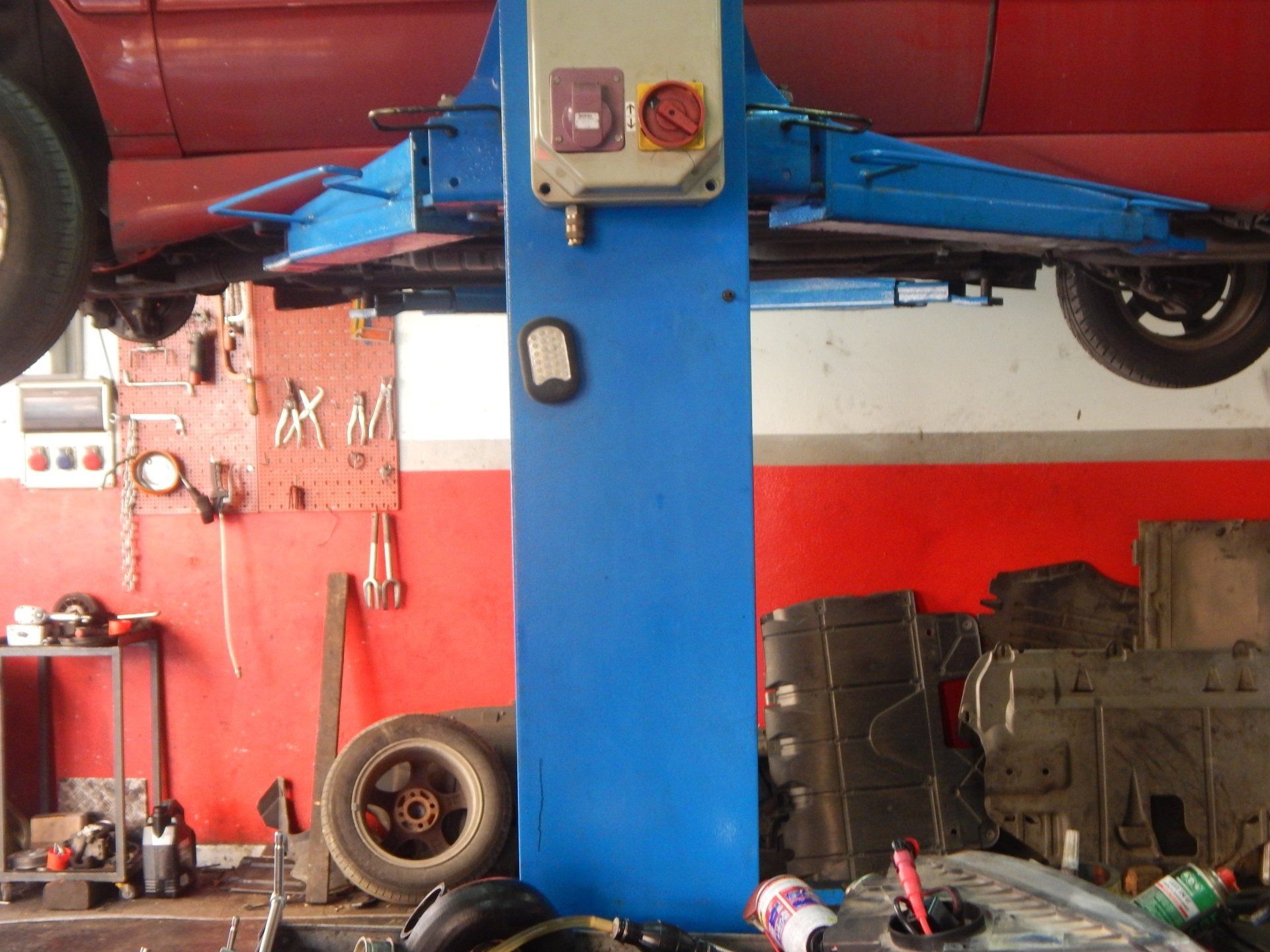 Blue car on a lift in an auto shop with red walls and garage tools.
