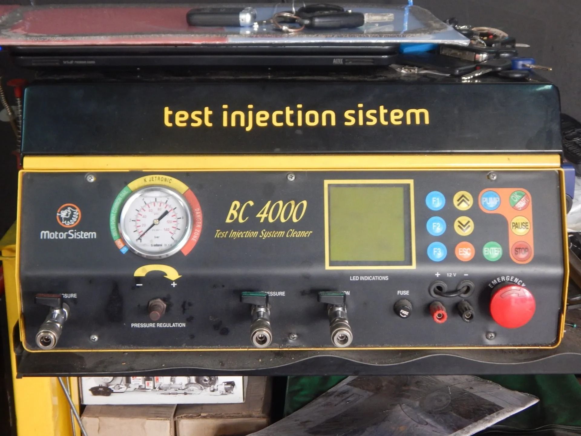 Test injection system machine with gauges, screen, buttons, and red emergency stop on a workbench