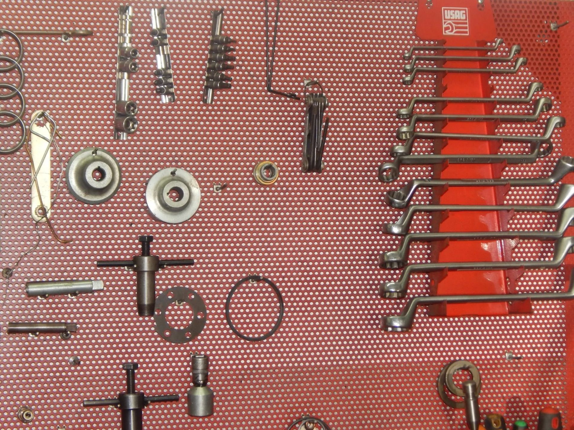 Assorted wrenches and tools arranged on a red pegboard wall in a workshop.