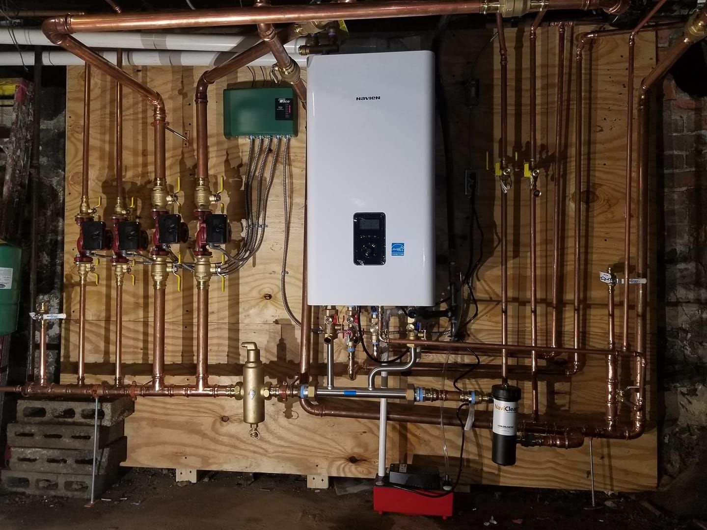 Copper pipes and valves connected to a white wall-mounted heating unit, on a wooden panel.