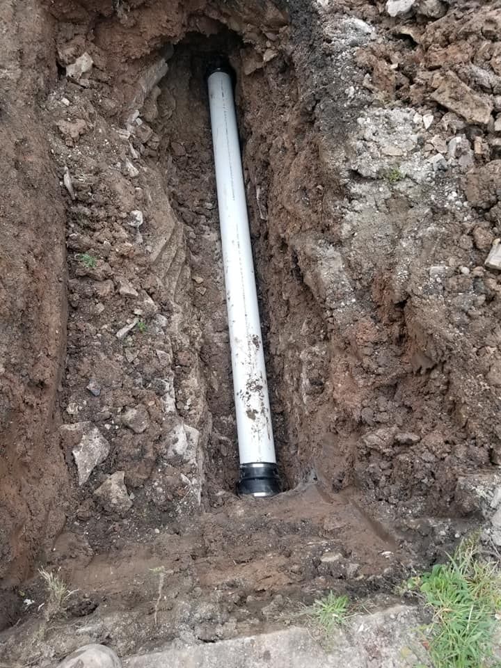 White pipe in a dirt trench, likely for plumbing or utilities.