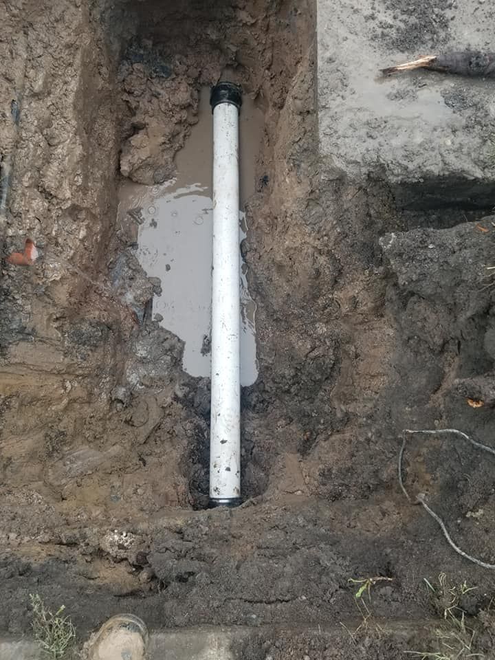 White PVC pipe in a rectangular trench, surrounded by dirt and concrete.