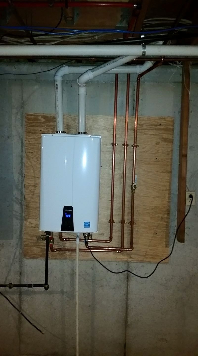 White tankless water heater on plywood, with copper pipes and electrical wiring in a basement.