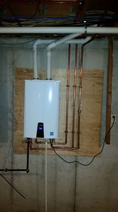 White tankless water heater on plywood, with copper pipes and electrical wiring in a basement.