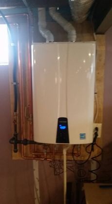 A wall-mounted, white tankless water heater with copper pipes in a basement.