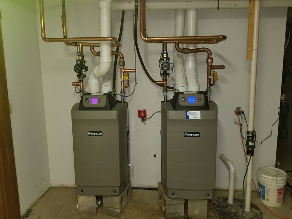 Two gray water heaters with copper pipes, set in a utility room.