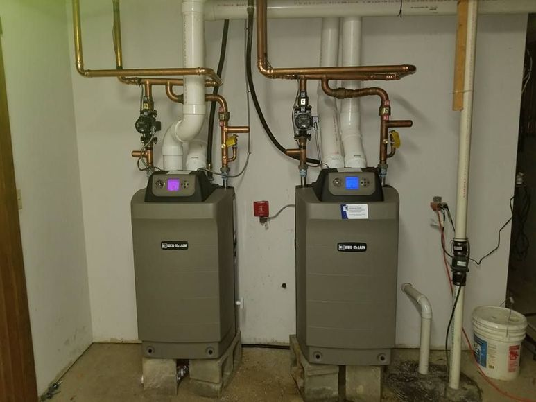 Two gray water heaters with copper pipes, set in a utility room.