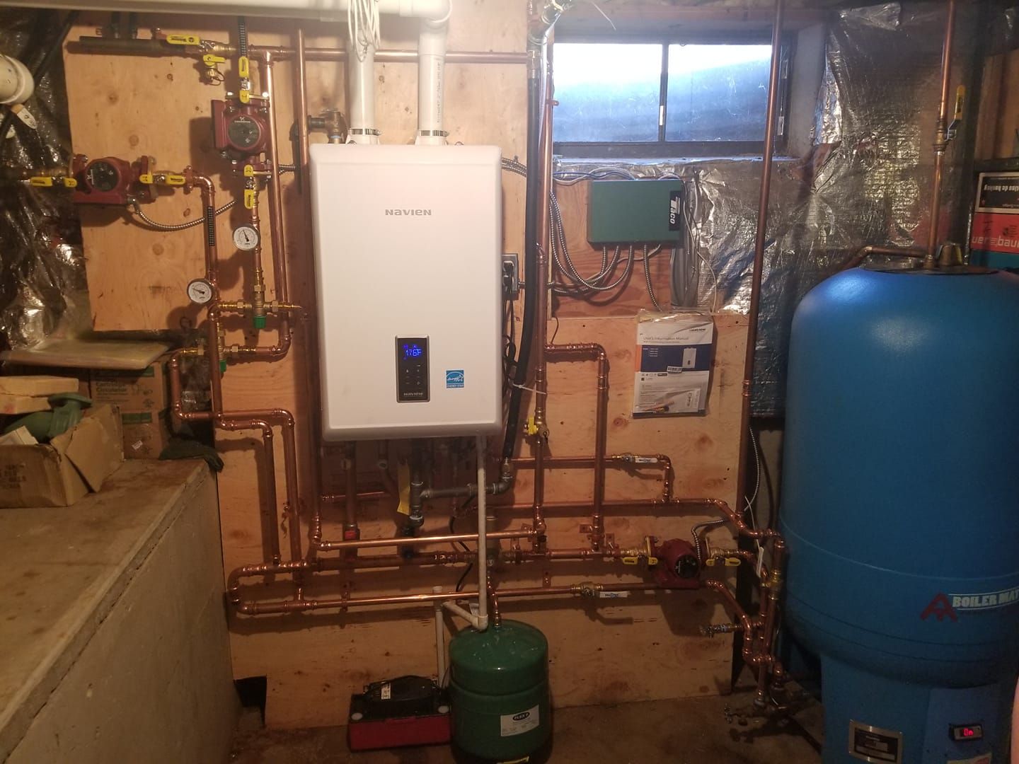 A utility room with a white water heater, copper pipes, a blue tank, and various other plumbing fixtures.