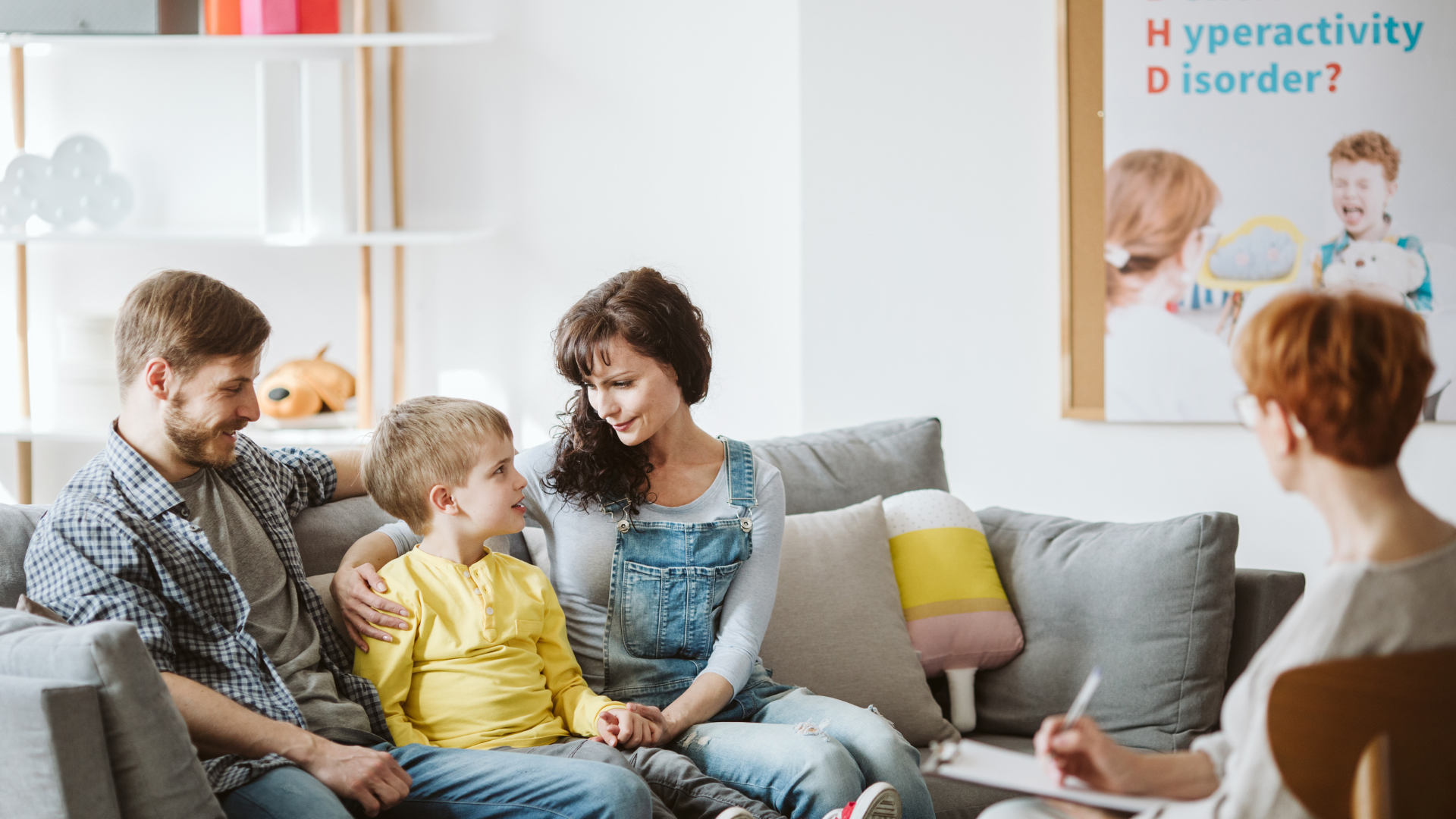 An elderly couple is sitting on a couch talking to a woman.
