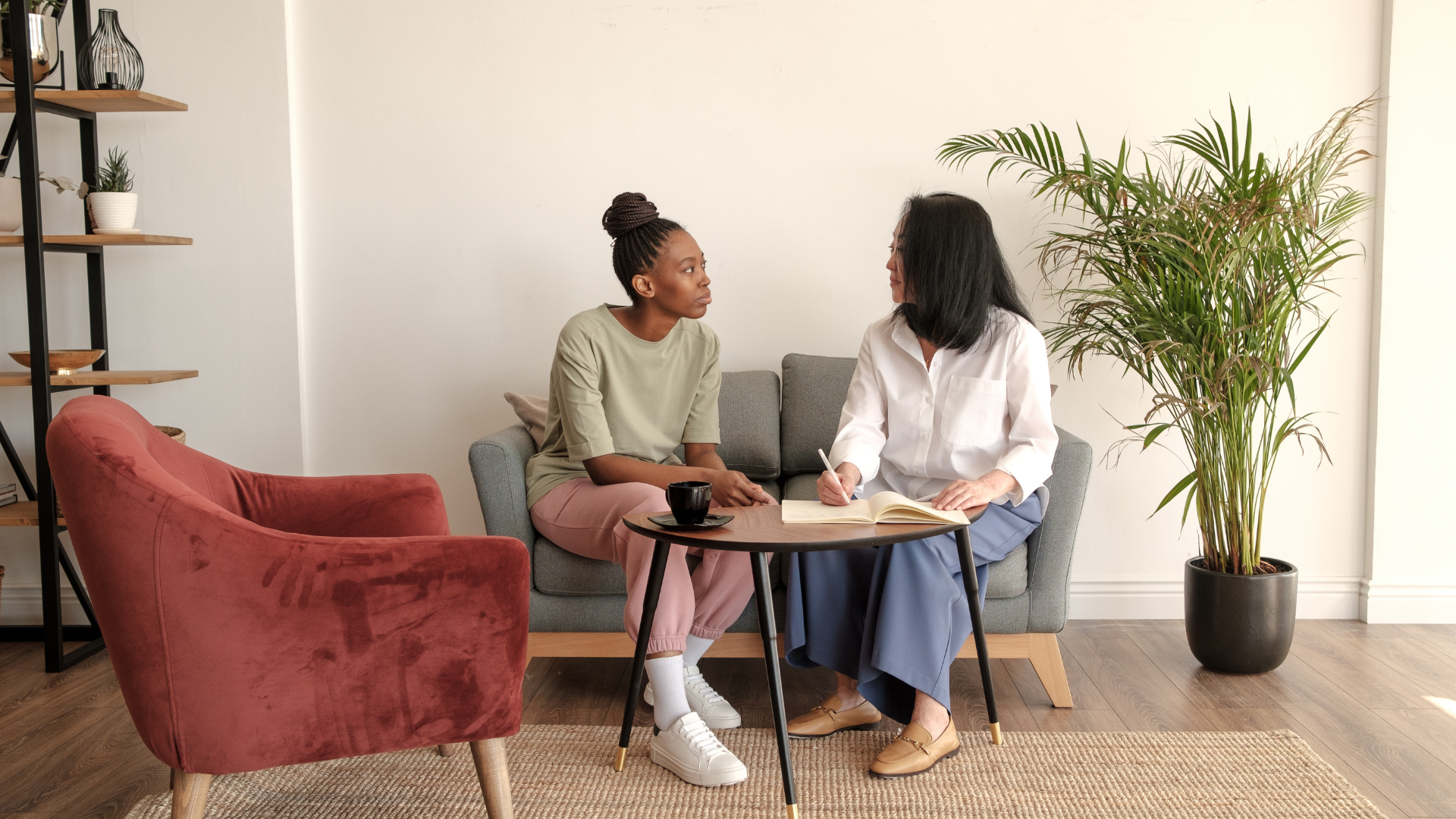 Two women are sitting on a couch talking to each other in a living room.