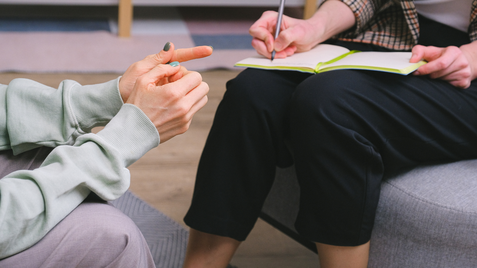 A woman is sitting on a couch talking to a man who is writing in a notebook.