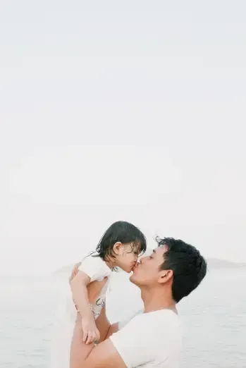 A man is holding a baby in his arms and kissing it on the cheek.