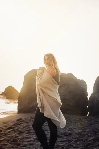 A woman is standing on a beach wrapped in a blanket.