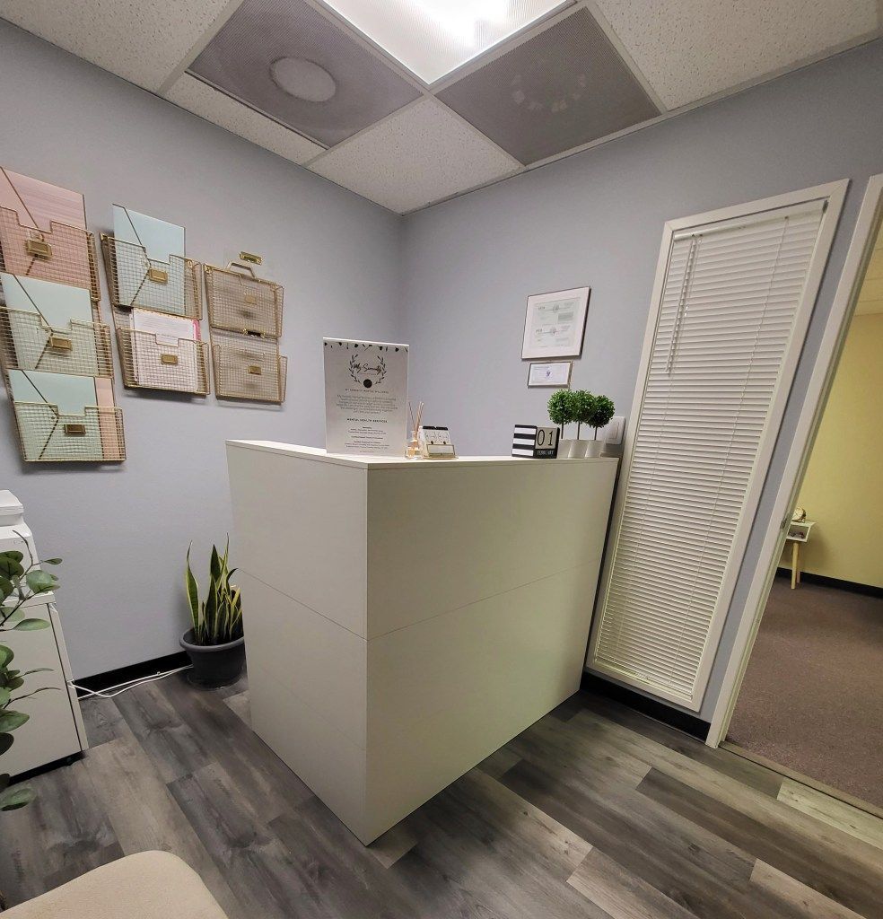 A room with a white desk and a plant on the floor