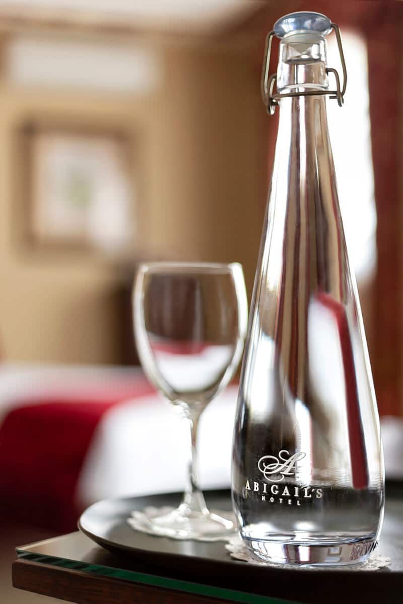 A bottle of water and a wine glass on a tray in a hotel room.
