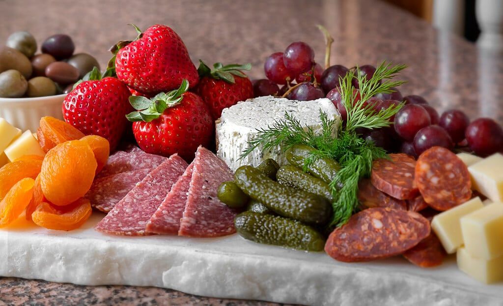 A marble cutting board topped with meat , cheese , grapes , strawberries and olives.