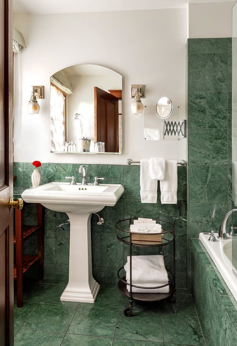 A bathroom with green tiles , a sink , a mirror and a tub.