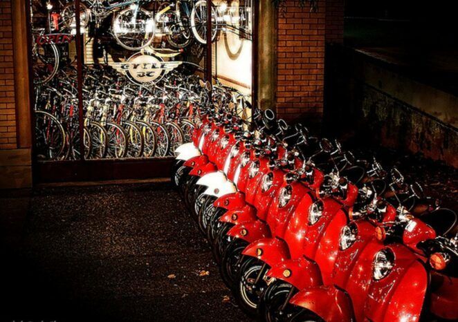 A row of red scooters are parked in front of a brick building