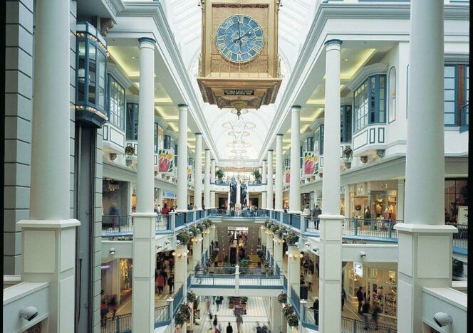 A large clock hangs from the ceiling of a shopping mall
