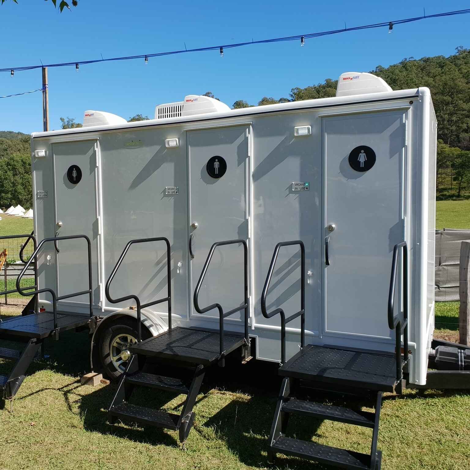 A Trailer With Three Toilets are Parked in a Grassy Field — Absoloo Hire Pty Ltd in Port Macquarie, NSW