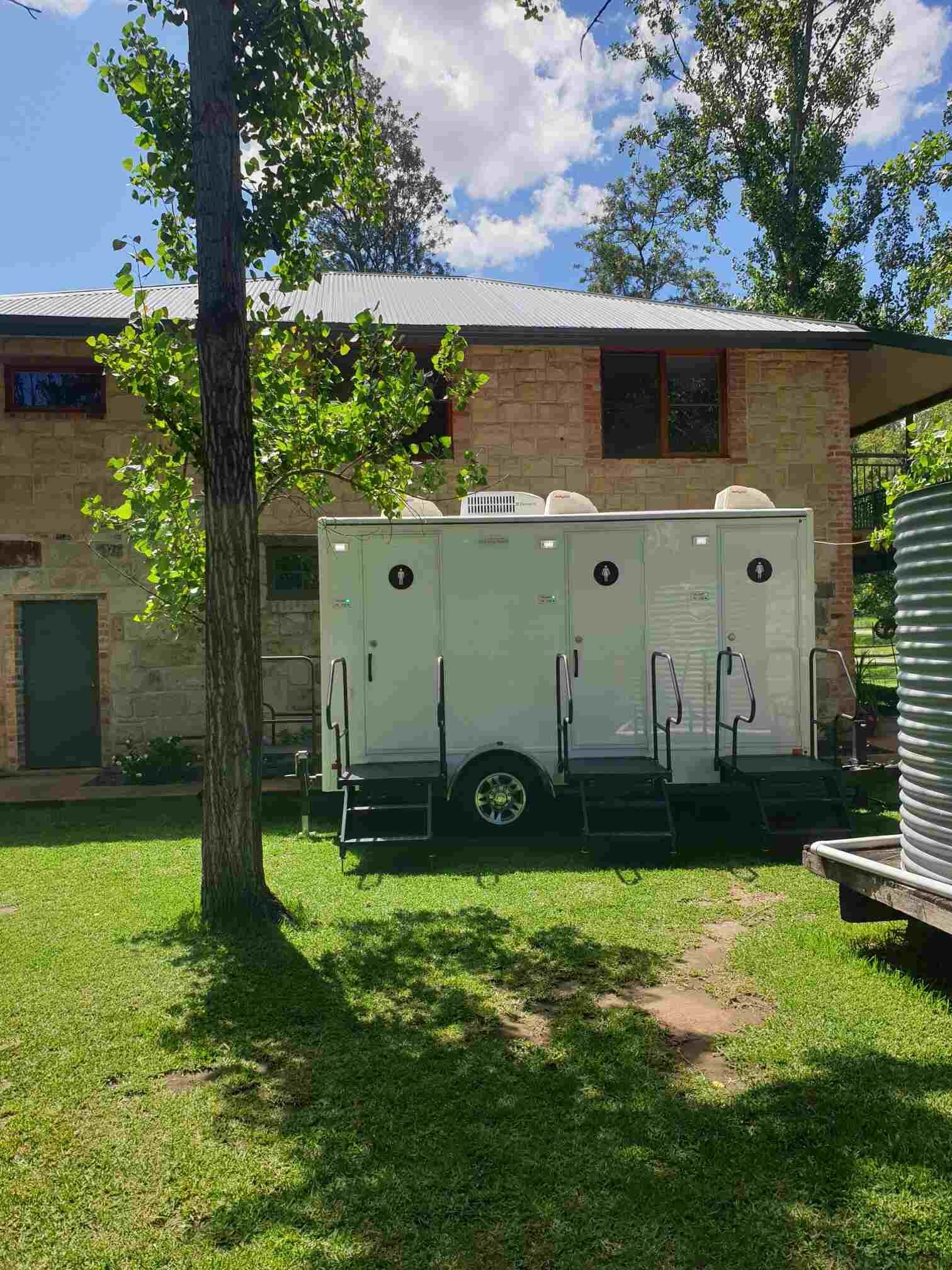 A Restroom is Parked in the Grass in Front of a House — Absoloo Hire Pty Ltd in Coffs Harbour, NSW