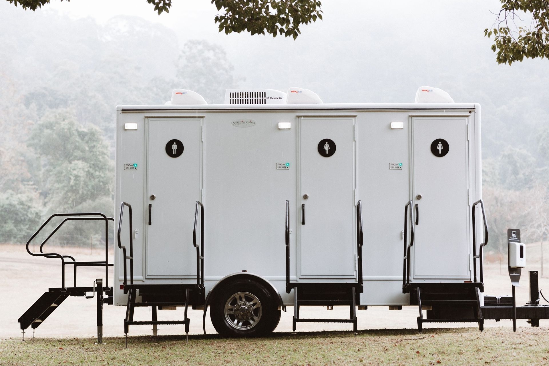 White portable restroom trailer with three stalls, on grass, outdoors — Absoloo Hire Pty Ltd In Morisset, NSW