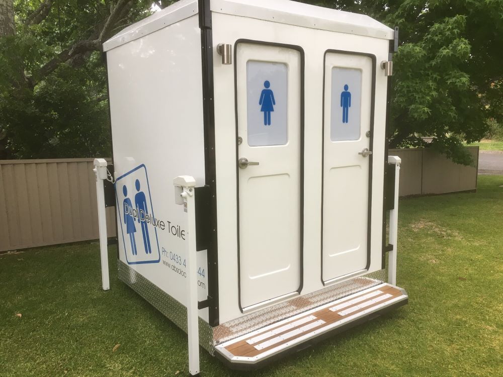A Portable Toilet is Sitting on Top of a Lush Green Field — Absoloo Hire Pty Ltd in Coffs Harbour, NSW