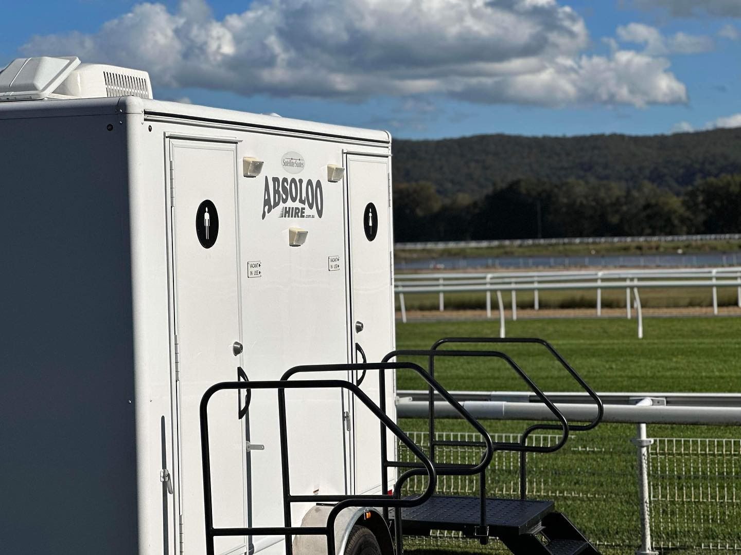 A Restroom With Stairs Leading Up to It is Parked in a Field — Absoloo Hire Pty Ltd in Newcastle, NSW