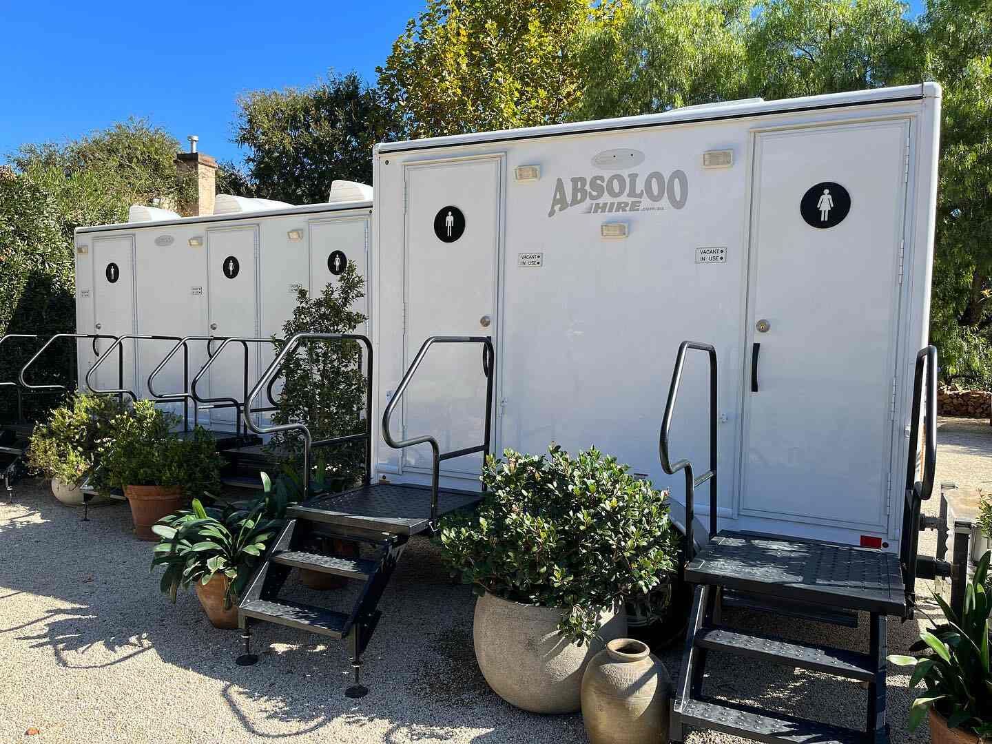 A Row of Restroom With Stairs and Potted Plants in Front of Them — Absoloo Hire Pty Ltd in Wyong, NSW