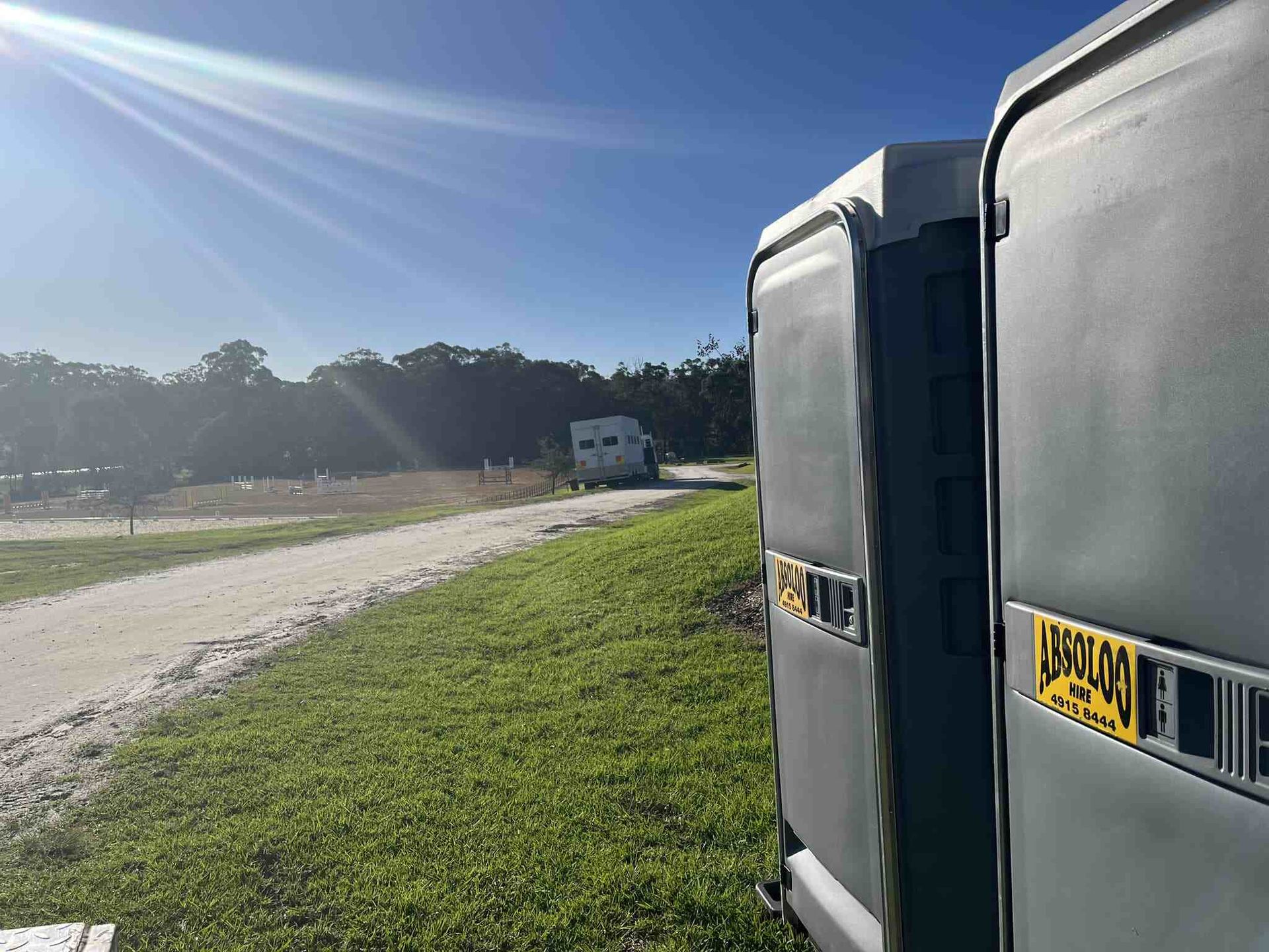 Two Portable Toilets Are Parked Next to Each Other in a Grassy Field — Absoloo Hire Pty Ltd in Port Macquarie, NSW