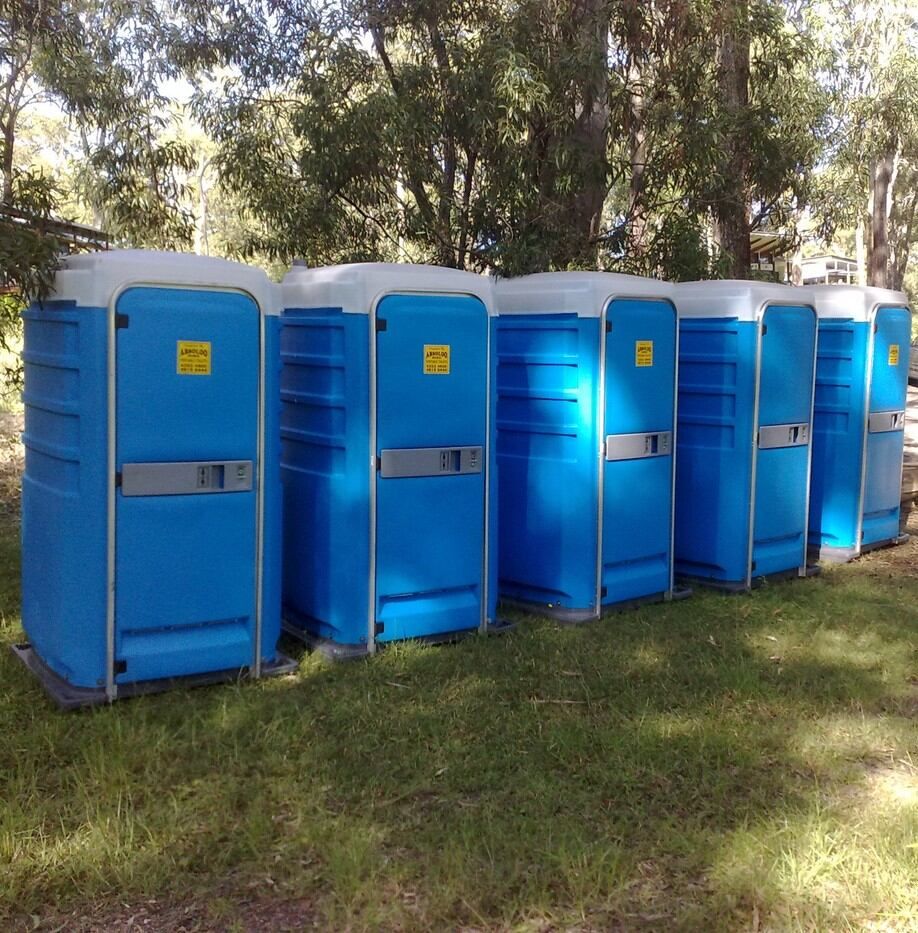 A Row of Portable Toilets Are Lined Up in the Grass — Absoloo Hire Pty Ltd in Wyong, NSW