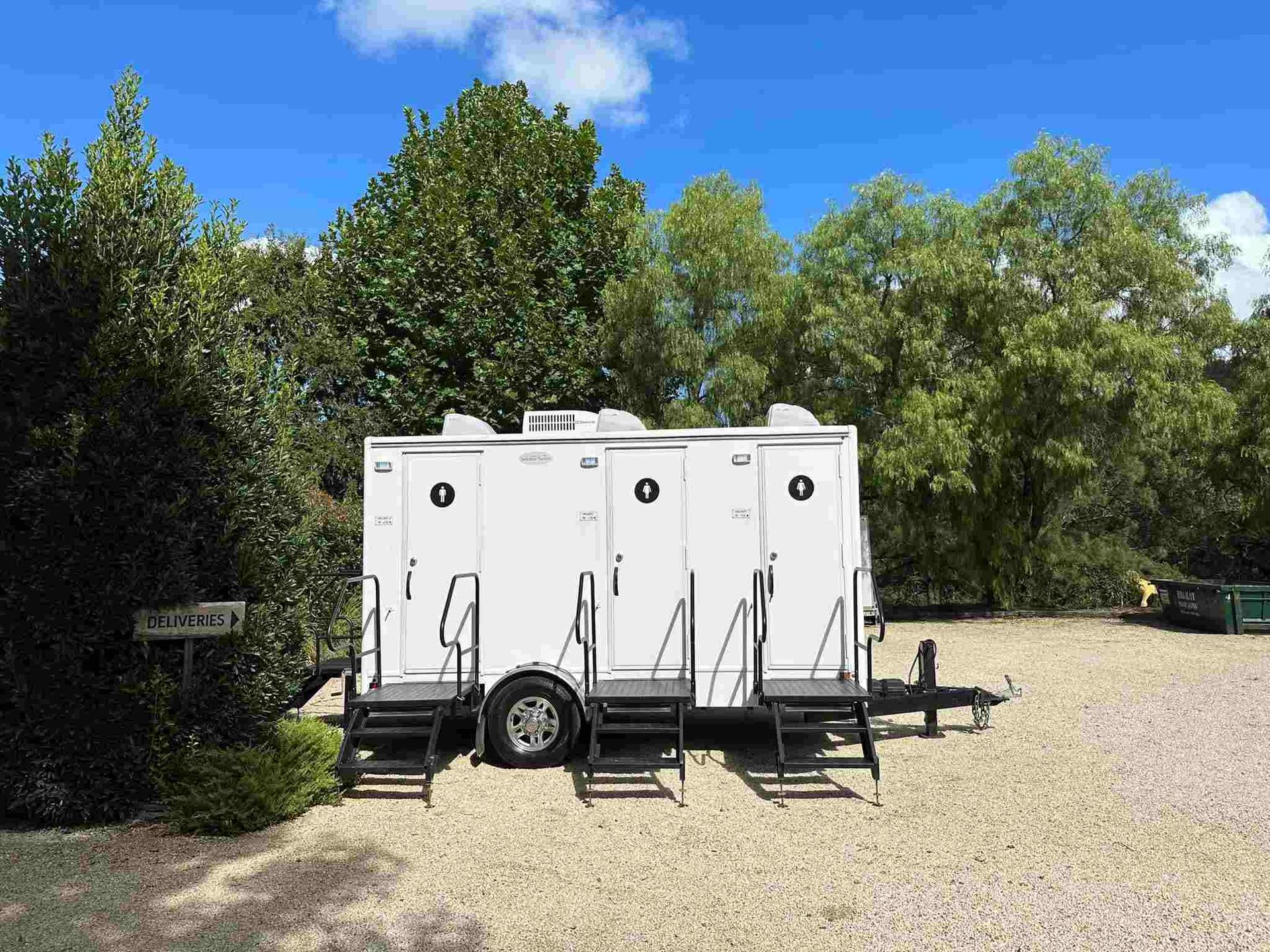 A Trailer With Three Toilets on It is Parked in a Gravel Lot — Absoloo Hire Pty Ltd in Wyong, NSW