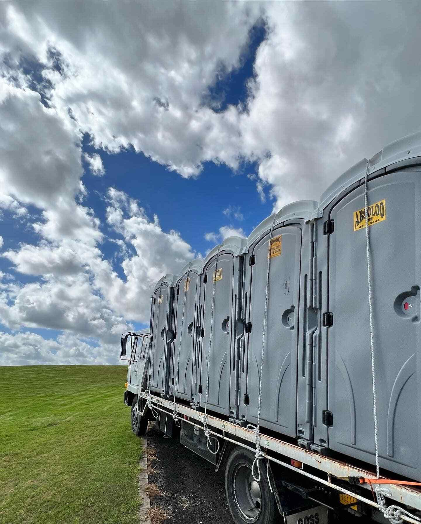 A Truck Filled With Portable Toilets is Parked in a Grassy Field — Absoloo Hire Pty Ltd in Morisset, NSW