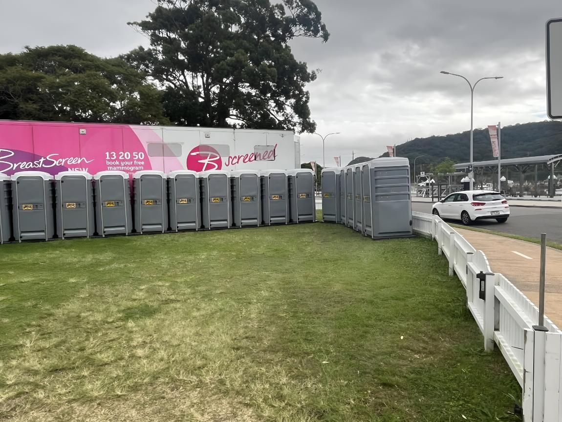 A Row of Portable Toilets Are Lined Up in a Grassy Field Next to a Road — Absoloo Hire Pty Ltd In Morisset, NSW