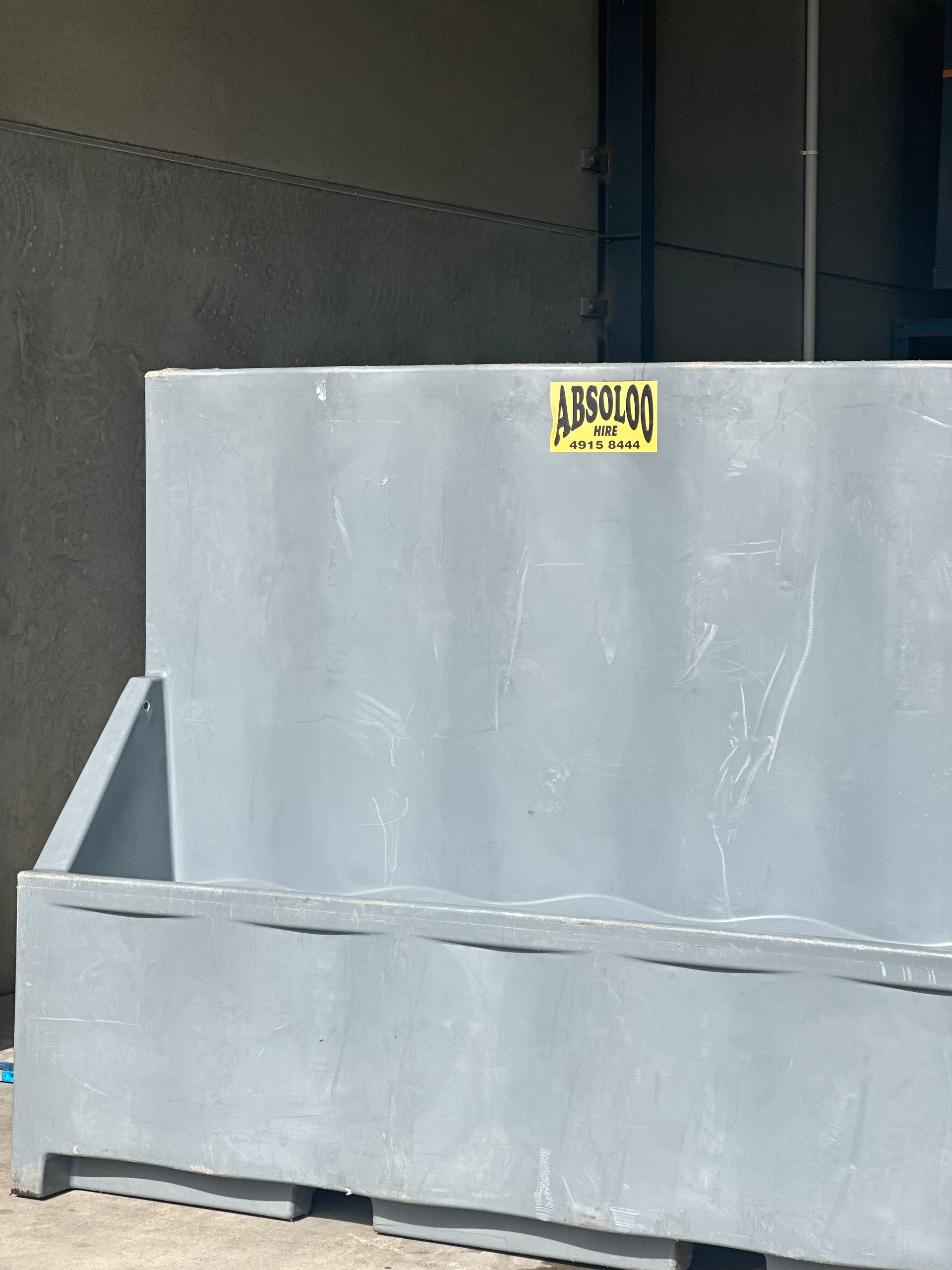 A Large Gray Container With a Yellow Sticker on It is Sitting in Front of a Building — Absoloo Hire Pty Ltd In Morisset, NSW