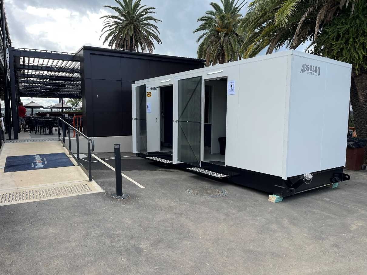 A White Toilet is Place in Front of a Building — Absoloo Hire Pty Ltd in Morisset, NSW