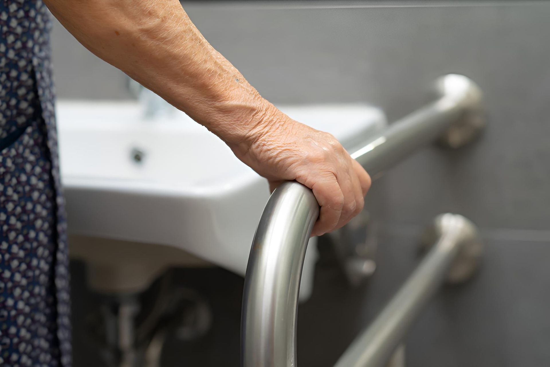 An Elderly Woman is Holding Onto a Railing in a Bathroom — Absoloo Hire Pty Ltd In Morisset, NSW
