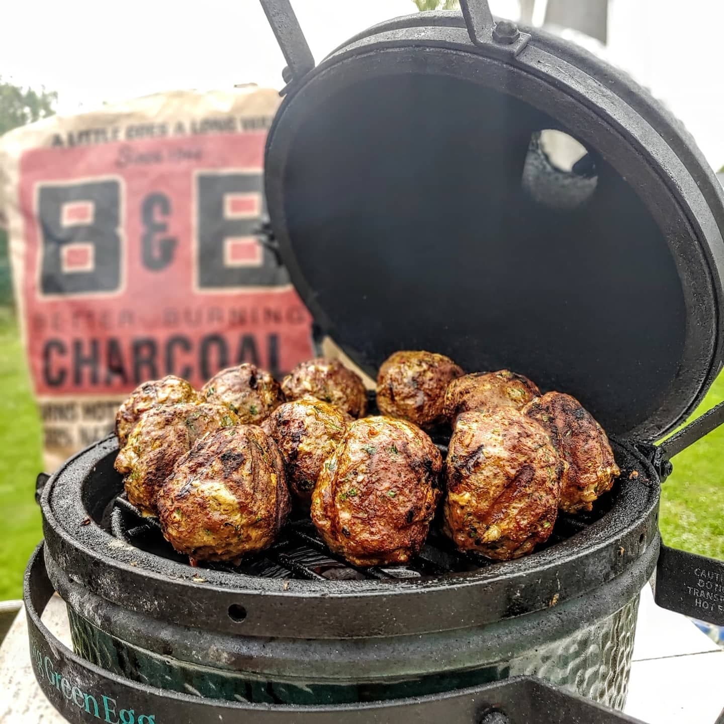 Image of grilled chicken on a ceramic grill with a bag of B&B Oak Lump charcoal in the background